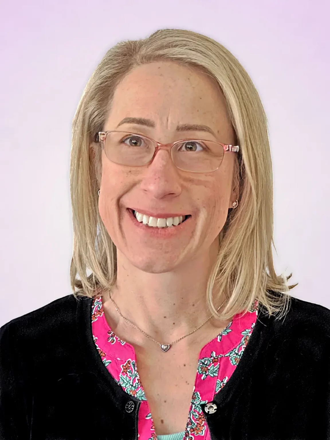 April Baker, a professional in arts and culture marketing, smiling warmly in a portrait with a soft lavender gradient background. She is wearing glasses, a black cardigan, and a floral blouse.